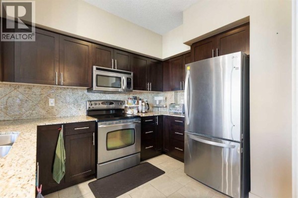 Kitchen with stainless steel appliances, granite countertops, and dark wood cabinets. - 1811, 8710 Horton Road Sw, Calgary