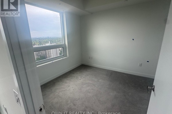 Empty bedroom with grey carpet, white walls, and a large window overlooking a city view. - 1811 - 4010 Eglinton Avenue W, Toronto
