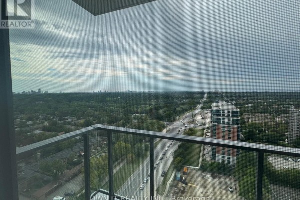 Balcony view overlooking a highway and cityscape with a tree-lined horizon and cloudy sky. - 1811 - 4010 Eglinton Avenue W, Toronto