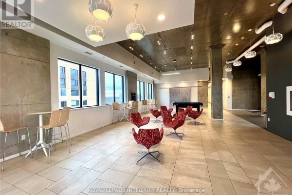 Common area lounge with red patterned chairs, white tables, bar seating, pool table, and large windows. - 1812 - 105 Champagne Avenue, Ottawa