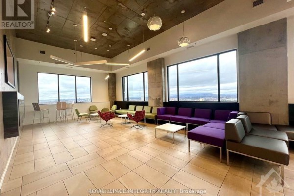 Spacious common area with modular purple sofas, white coffee table, green chairs, and city views. - 1812 - 105 Champagne Avenue, Ottawa