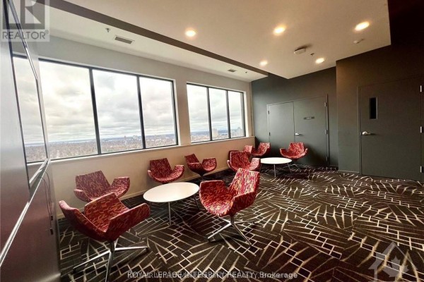 Seating area with red patterned chairs, white circular tables, and panoramic city views through large windows. - 1812 - 105 Champagne Avenue, Ottawa