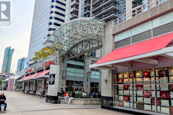 Street-level view of building entrance with shops and seating areas. - 1812 - 4978 Yonge Street, Toronto