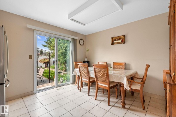 Dining area with a table set for six, wooden chairs, tile flooring, and a sliding glass door to the backyard. - 18126 98 Av Nw, Edmonton