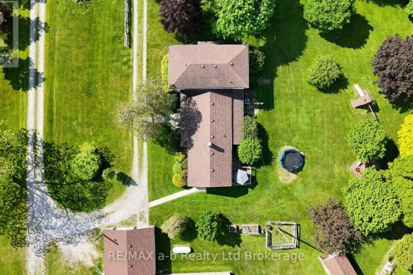 Top-down aerial view of a farmhouse roof and surrounding yard with trees and outbuildings. - 1813 Norfolk County 19 Road W, Norfolk