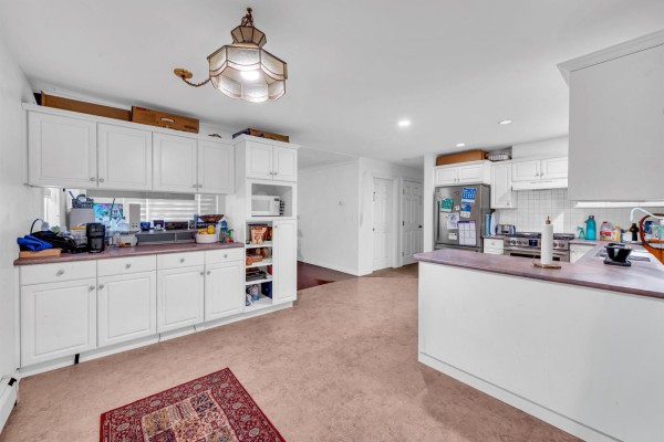A bright white kitchen with laminate countertops and stainless steel appliances faces a long counter with overhead cabinets. - 18136 Claytonwood Crescent, Surrey
