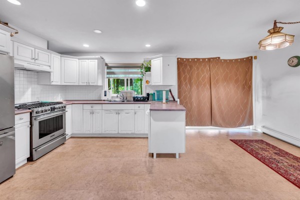The spacious white kitchen features white cabinets, stainless steel appliances, and a pink countertop island with large sliding doors. - 18136 Claytonwood Crescent, Surrey