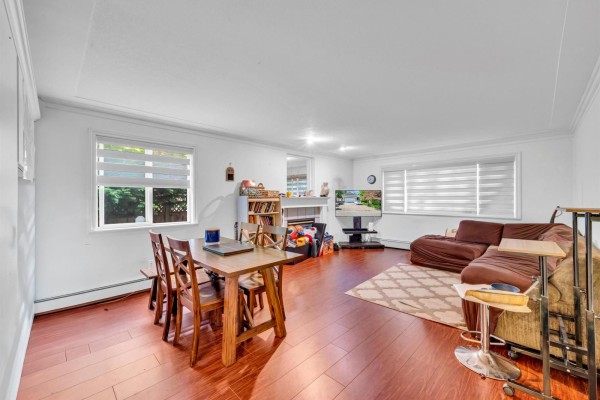 A living area with a dining table, sectional sofa, television, and hardwood floors has windows with blinds. - 18136 Claytonwood Crescent, Surrey