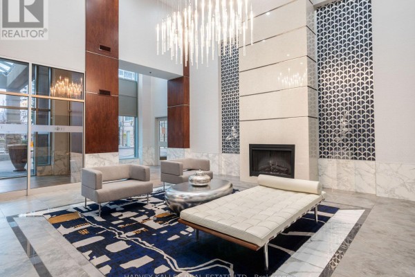 Building lobby with modern furniture, a fireplace, a decorative rug, and a large chandelier. - 1814 - 17 Barberry Place, Toronto