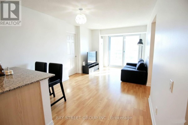 Living area with light wood floors, white walls, a black sofa, and a sliding glass door. - 1814 - 83 Borough Drive, Toronto