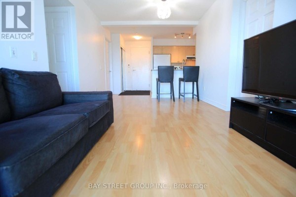 Open concept living space with light wood floors, a navy sofa, and a kitchen counter with stools. - 1814 - 83 Borough Drive, Toronto