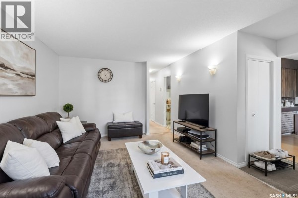 Living room with a large brown leather sofa, white coffee table, and television. - 1814 Wilson Crescent, Saskatoon
