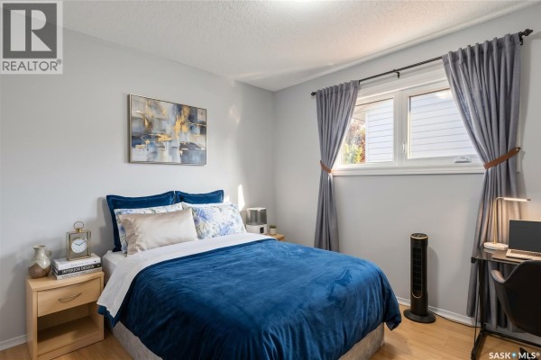Bedroom with a queen-size bed, nightstand, and a desk with a laptop. - 1814 Wilson Crescent, Saskatoon
