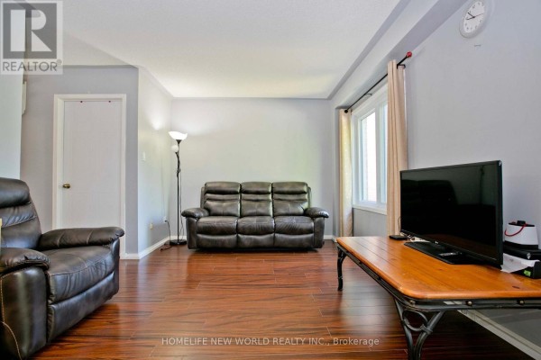 Living room with hardwood floors, beige curtains, sofa, armchair, and a television on a coffee table. - 1814 Woodgate Court, Oshawa