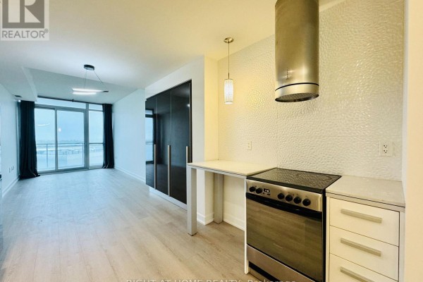 Kitchen counter with stovetop, stainless steel hood vent, and white textured wall. - 1815 - 38 Dan Leckie Way, Toronto