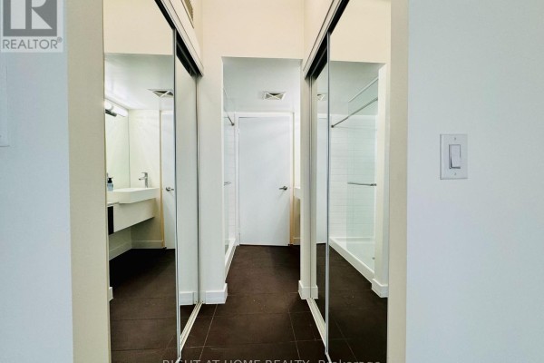 Hallway with dark tiled floor, mirrored closet doors, and bathroom entrance. - 1815 - 38 Dan Leckie Way, Toronto
