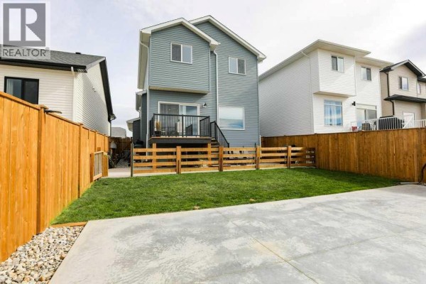 Rear exterior of a two-story house with blue siding, a deck, and a fenced backyard with grass. - 182 Caribou Bend N, Lethbridge