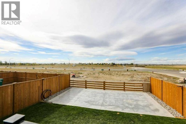 View from a fenced backyard showing a concrete patio, grass, and a wide open landscape beyond. - 182 Caribou Bend N, Lethbridge