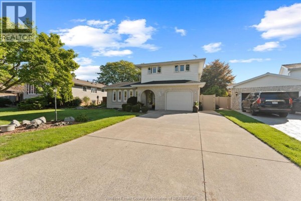 Wide view of the front exterior and driveway of a two-story white brick house in Tecumseh. - 182 Centennial, Tecumseh