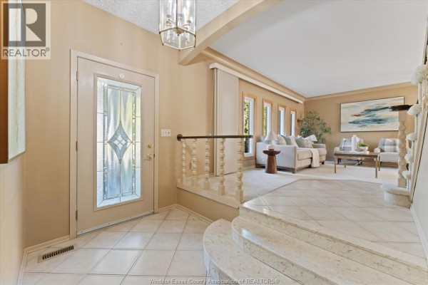 View from the foyer showing the entryway, staircase, and a living room with light furniture. - 182 Centennial, Tecumseh