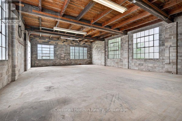 Interior view of an empty commercial space with concrete floor, cinder block walls, and large windows. - 182 Chatham Street, Hamilton