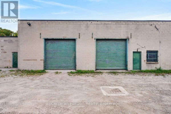 Rear exterior view of a commercial building with two green roll-up garage doors and adjacent doors. - 182 Chatham Street, Hamilton
