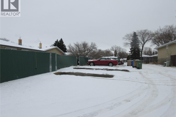 Driveway with a red car, trash bins, and chain-link fence. - 182 Rothwell Crescent, Regina