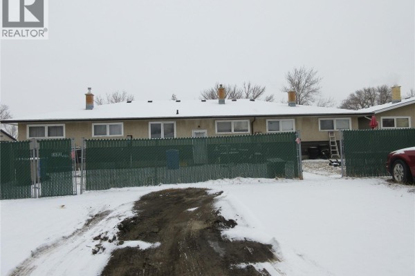 Back exterior of the townhouse complex with snow and chain-link fencing. - 182 Rothwell Crescent, Regina