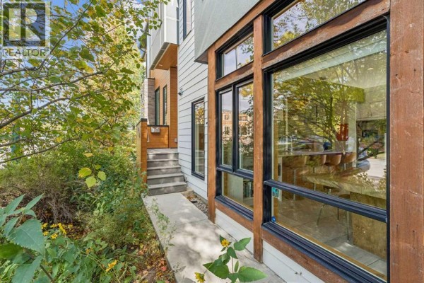 Concrete walkway leading to stairs and large windows of the duplex, surrounded by plants. - 1820 4 Street Ne, Calgary