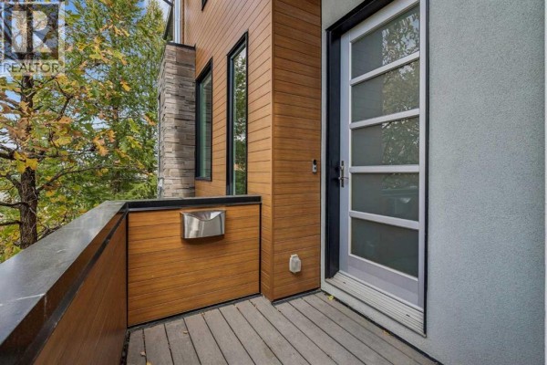Covered balcony area with wood decking, wood paneling, and a glass-paneled front door. - 1820 4 Street Ne, Calgary