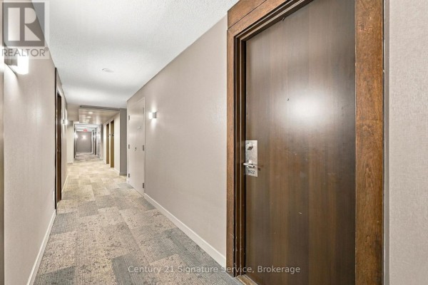 Long apartment building hallway with beige walls, patterned carpet, and numerous wooden doors. - 1822 - 135 Village Green Square, Toronto