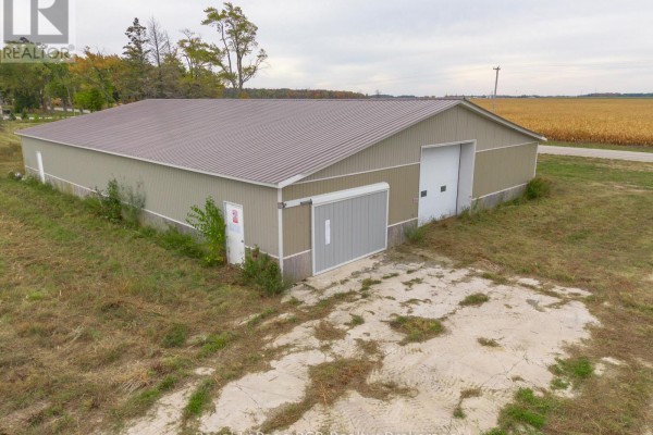 Side view of a tan commercial building with metal siding and a grey roll-up door next to a white garage door. - 1822 Concession 12 Concession, Huron Kinloss