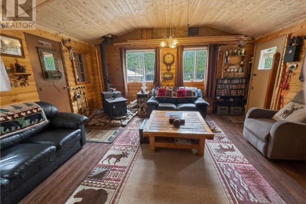 Living room with wood-paneled walls, wood stove, sofas, and a wooden coffee table. - 18246 Highway 540, Evansville