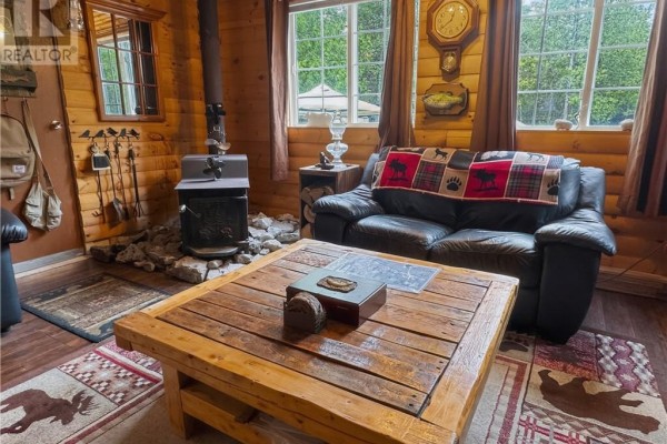 View of the living room featuring a black leather sofa, wood stove, and a rustic coffee table. - 18246 Highway 540, Evansville