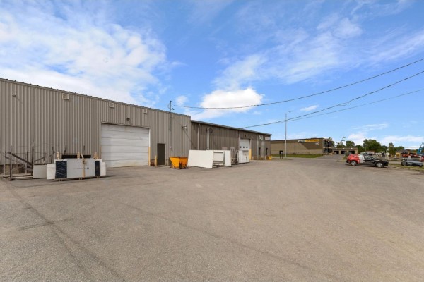 Exterior of a commercial building with a large garage door, asphalt lot, and material slabs. - 183 Boul. De L'aéroport, Gatineau
