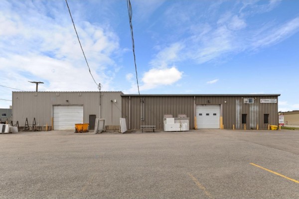 Rear exterior of a commercial building with two garage doors and metal paneling. - 183 Boul. De L'aéroport, Gatineau