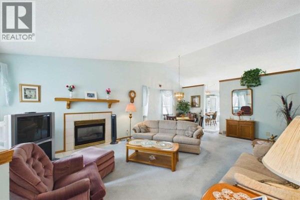 Living room with pale blue walls, vaulted ceiling, gas fireplace, sofa, and dining area. - 183 Doran Crescent, Red Deer
