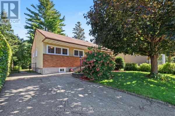 Side exterior of a bungalow with brick accents and a paved driveway on a sunny day. - 183 Martin Avenue, Ottawa