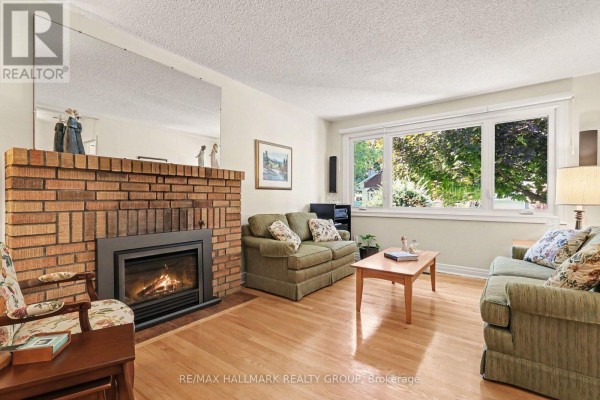 Living room with a brick fireplace, wood floors, two sofas, and a large window. - 183 Martin Avenue, Ottawa