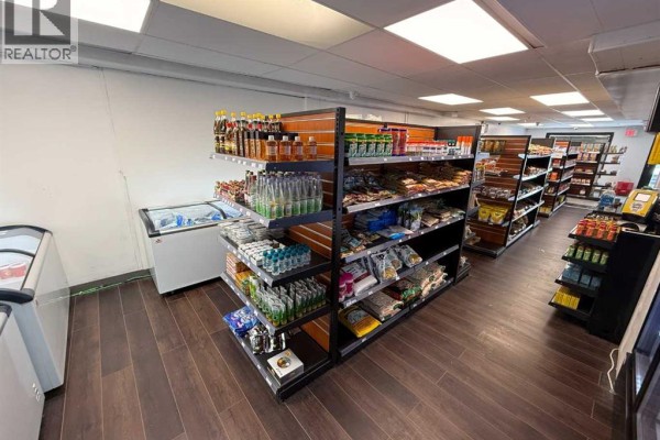 Commercial space with rows of shelves displaying snacks and packaged goods, dark wood floors, and exit signs. - 183 Pembina Avenue, Hinton