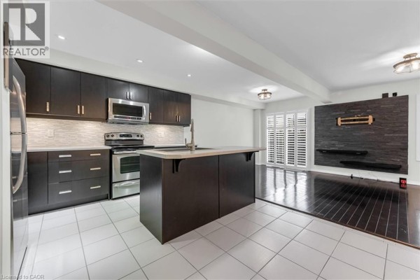 Modern kitchen with dark cabinetry, stainless steel appliances, and stone accent wall. - 183 Penny Lane, Stoney Creek