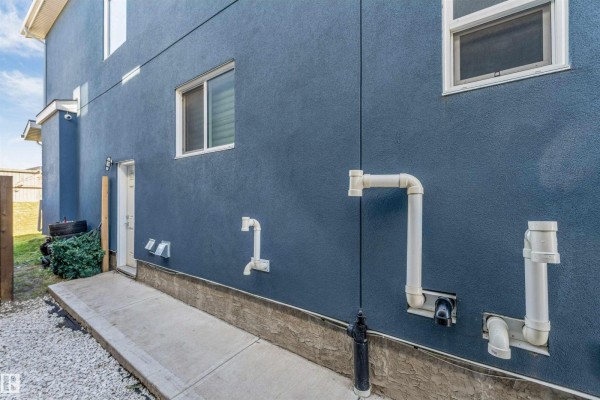 Exterior wall of the house with multiple white PVC pipes and windows. - 1831 18 St Nw, Edmonton