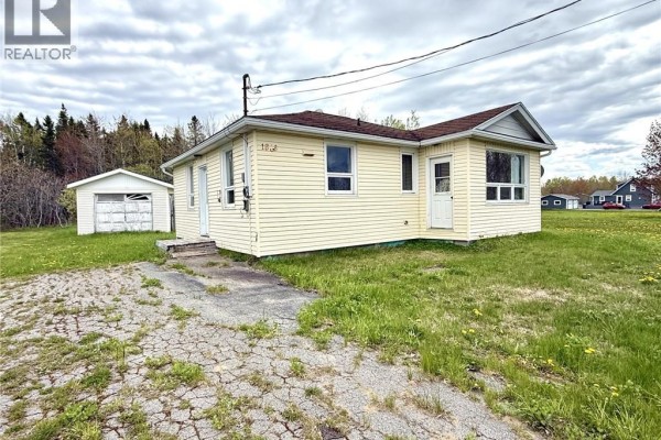 Exterior view of the pale yellow bungalow with a detached garage, surrounded by green grass and trees. - 1833 Route 335, Saint Simon