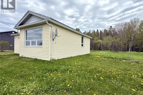 Rear right exterior view of the pale yellow bungalow with a large window, showing a woodsy background. - 1833 Route 335, Saint Simon