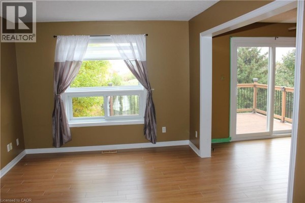 Interior view of a living room with tan walls, wood laminate flooring, and a large window. - 184 Northampton Crescent Unit# B, Waterloo
