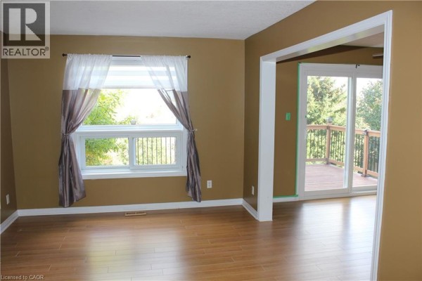 Interior view of a living room with tan walls, wood laminate flooring, and a sliding glass door to a deck. - 184 Northampton Crescent Unit# B, Waterloo