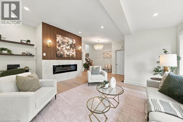Living room with a fireplace, wood accent wall, modern furniture, and glass coffee tables. - 184 Torresdale Avenue, North York