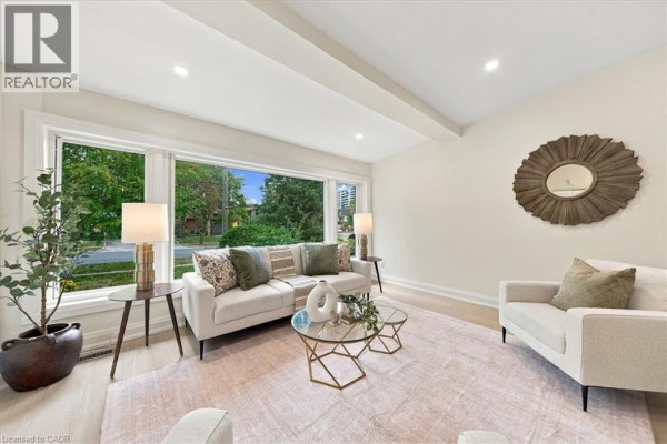 Bright living room with a large bay window, beige sofas, and a decorative wall mirror. - 184 Torresdale Avenue, North York