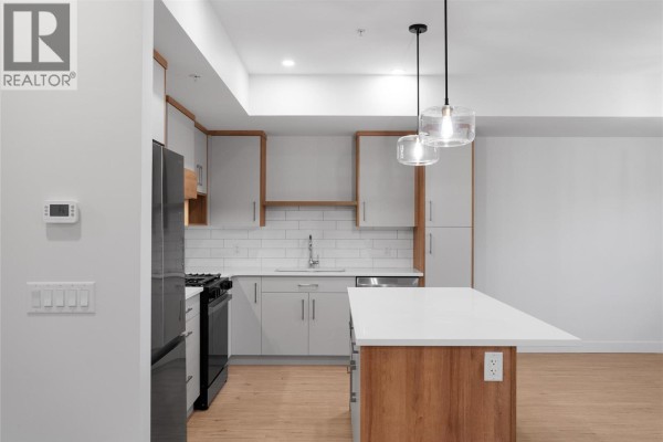 Living room with light wood flooring, white walls, electric fireplace, and a balcony door. - 1844 Qu'appelle Boulevard Unit# 203, Kamloops