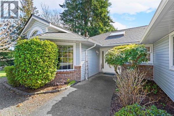 Pathway leading to the front entrance of a light blue house with large green bushes. - 1848 Amelia Cres, Nanoose Bay